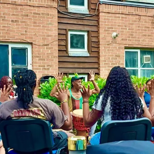 Students and an instructor learning how to drum in a workshop sat outside